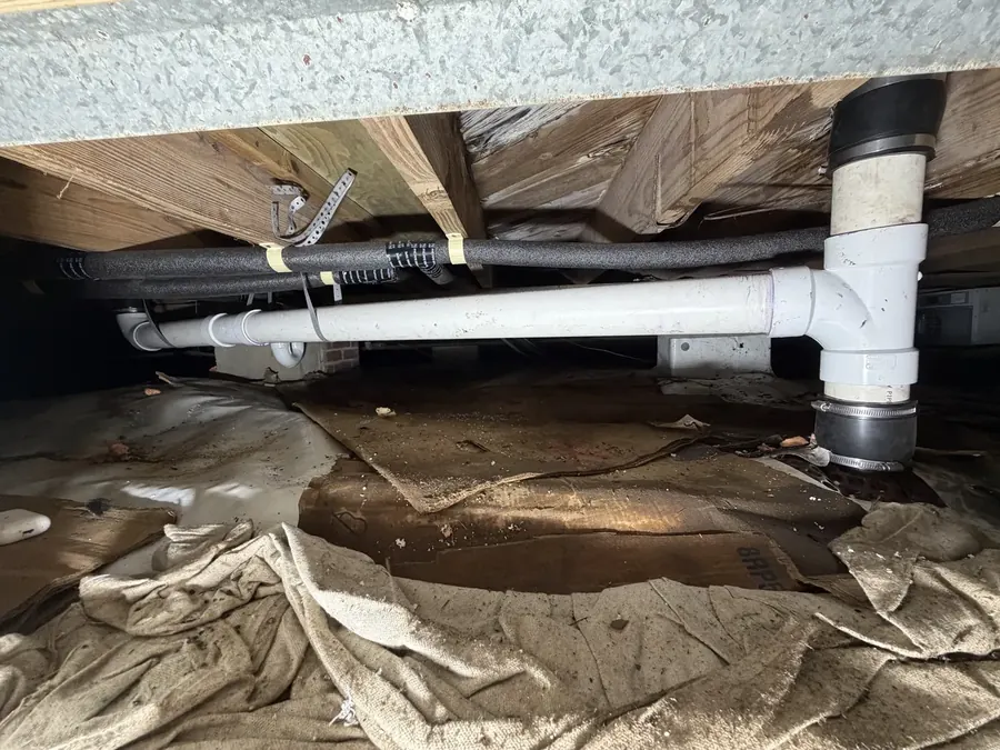 New white PVC drain line connected to a vertical drain under a raised home