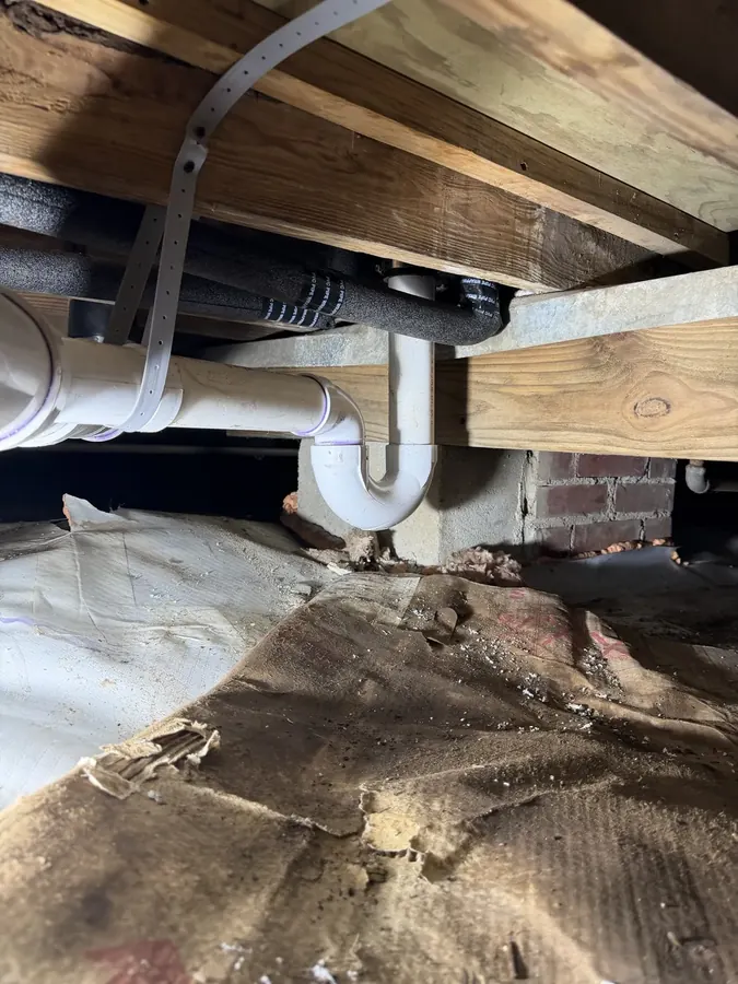 New PVC P-trap and drain line strapped to floor joists in a crawlspace