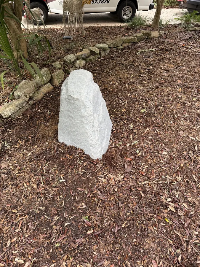 Artificial rock cover in a mulched garden bed hiding the water treatment unit