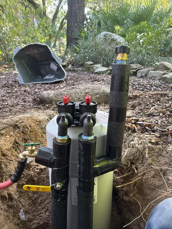 Outdoor water treatment unit with black insulated pipes, a shutoff valve and a hose connection