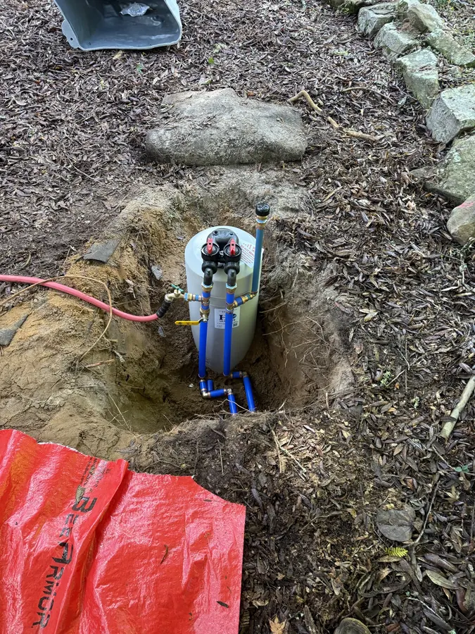 Water treatment unit set in a hole in a garden bed with new blue supply lines