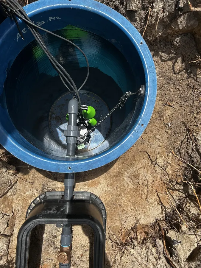 Open pump basin in the ground showing the pump discharge pipe, float switches and valve