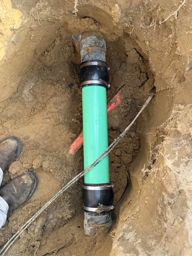 New green sewer pipe joined to an old sewer line with shielded couplings in an open trench