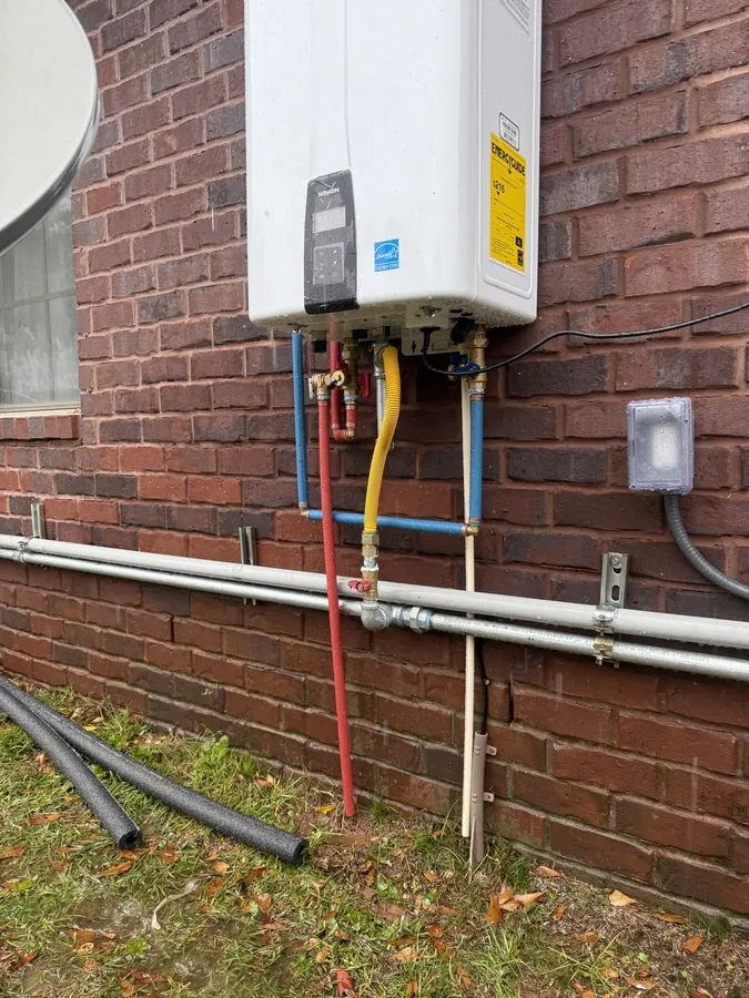 Gas line, water lines and electrical outlet connected below an outdoor tankless water heater on brick