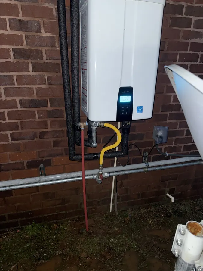 Outdoor tankless water heater powered on at dusk with insulated water lines