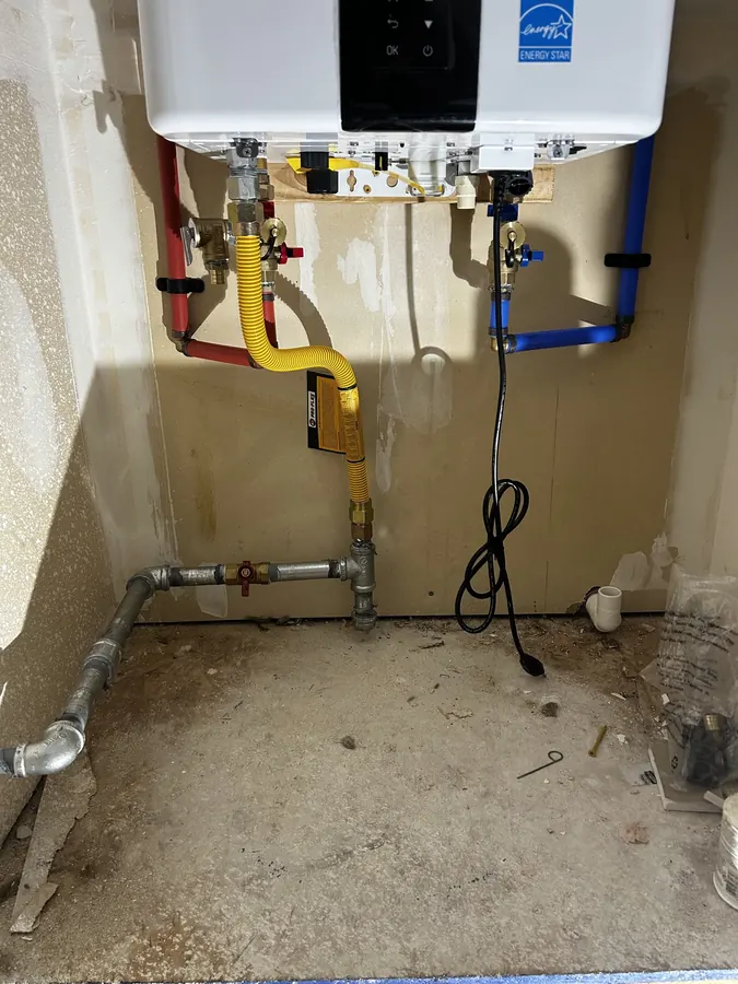 Gas line, shutoff valves and red and blue water lines connected under a wall-hung tankless water heater