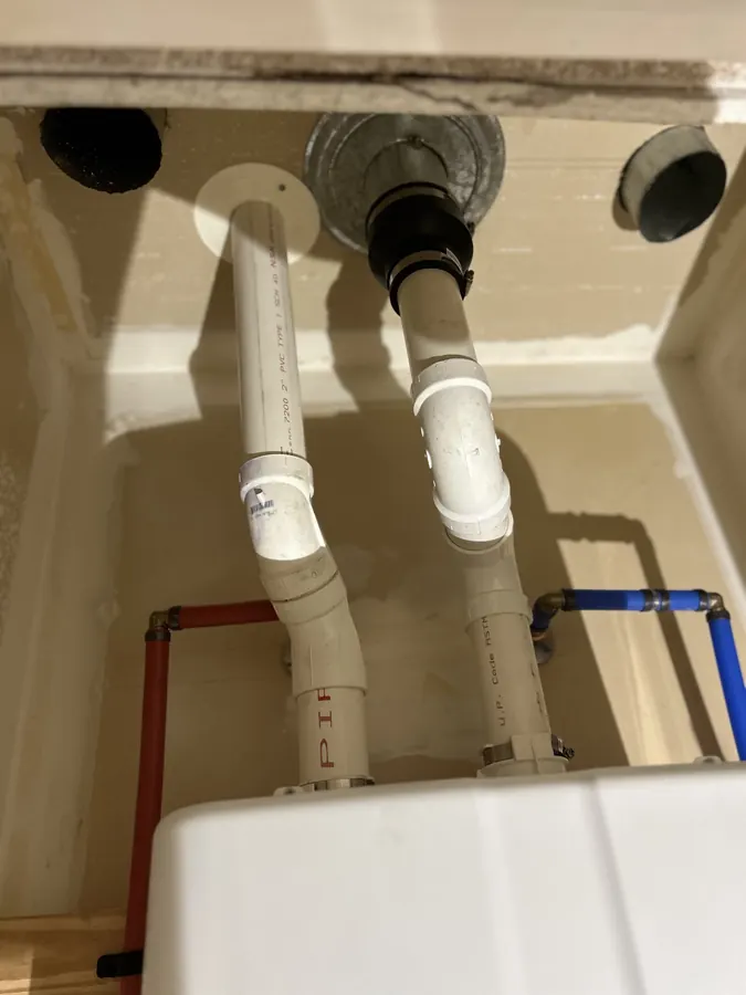 White PVC vent and intake pipes running from the top of a tankless water heater through the ceiling