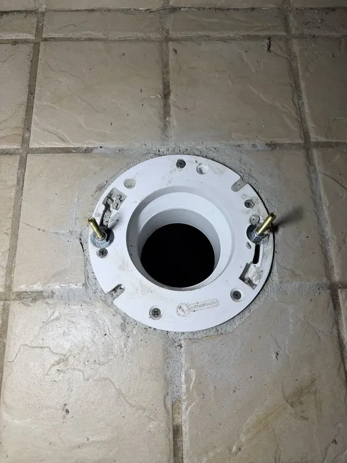 New white toilet flange with brass bolts set in a stone tile floor