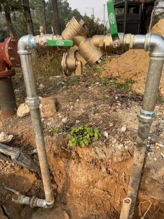 Large brass backflow preventer with green-handled shutoff valves on two galvanized risers in an open excavation