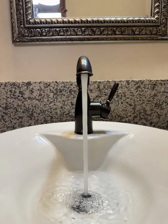 New oil-rubbed bronze bathroom faucet running into a white sink