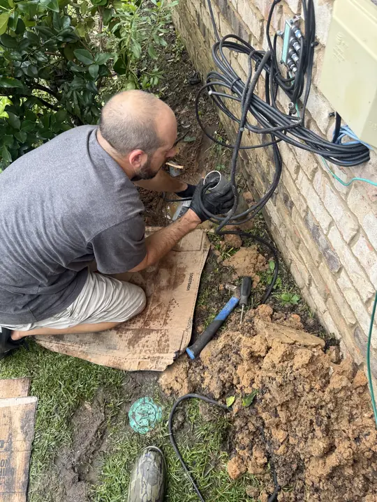 A Golden Plumber team member kneeling and digging by hand beside a brick home