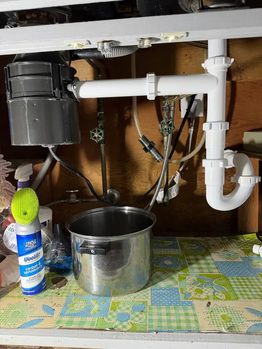 New white PVC trap and drain arm connected to a garbage disposal under a kitchen sink