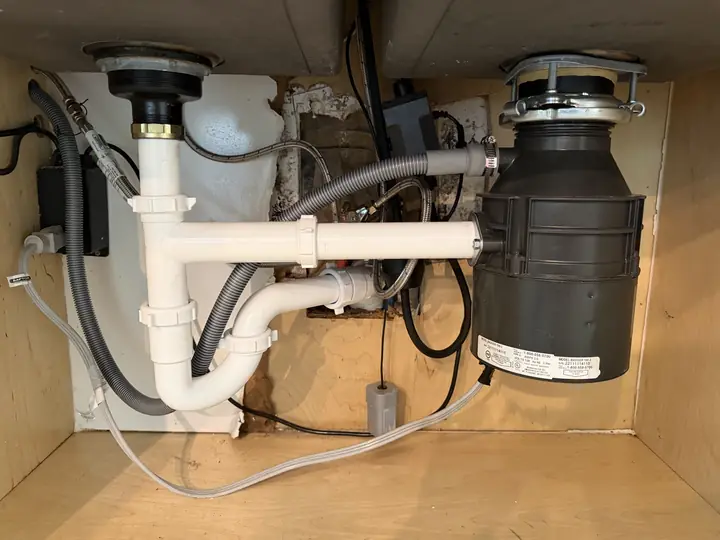 New garbage disposal and white PVC drain piping under a kitchen sink