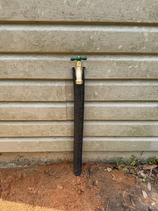 New brass hose bib on an insulated riser against house siding