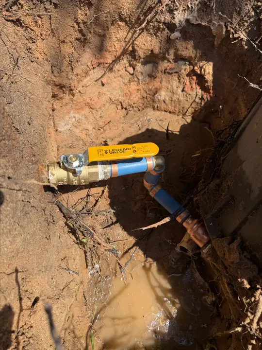 New brass ball valve with yellow handle on a blue water service line in an excavated hole