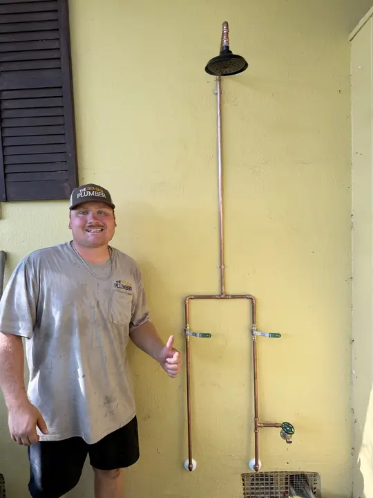 A Golden Plumber team member giving a thumbs up beside a new exposed copper outdoor shower
