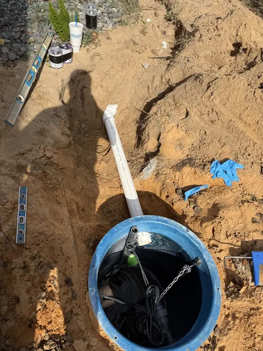 New pump basin with pump and float set in an open excavation with a PVC line and levels beside it