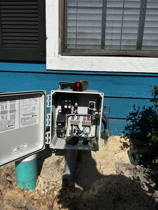 Open pump control panel with alarm light mounted on the side of a house