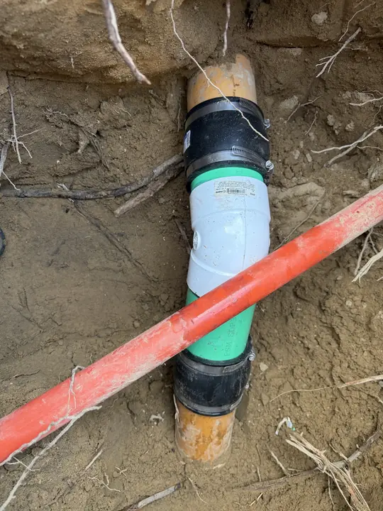 New sewer pipe section with couplings tied into an old clay sewer line in a trench