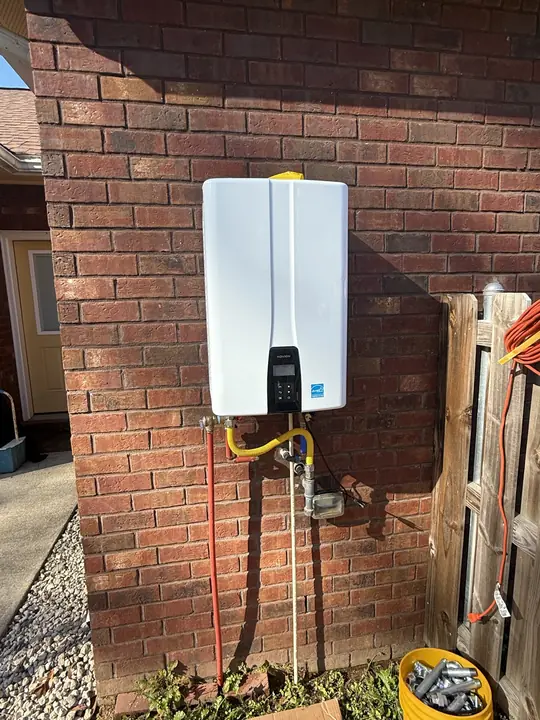 Outdoor tankless water heater mounted on a brick wall with gas and water lines below