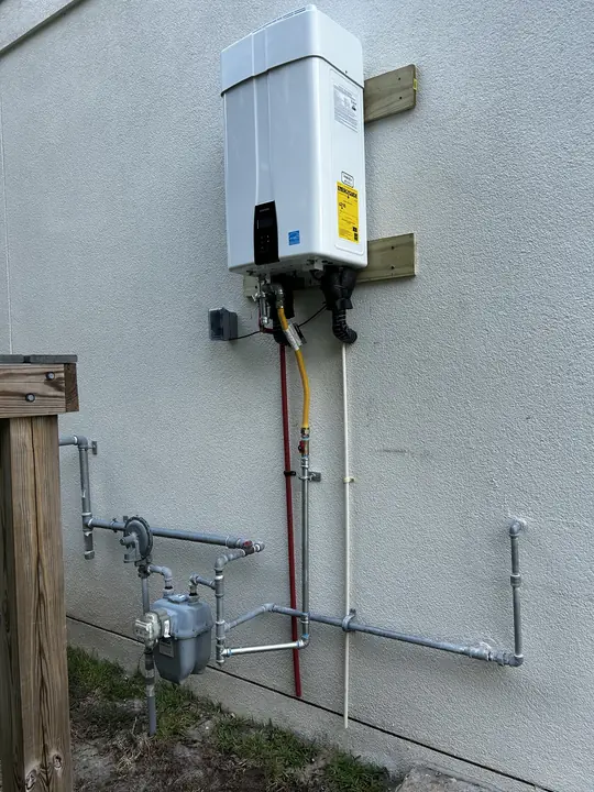 Outdoor tankless water heater on a stucco wall with new gas piping from the gas meter
