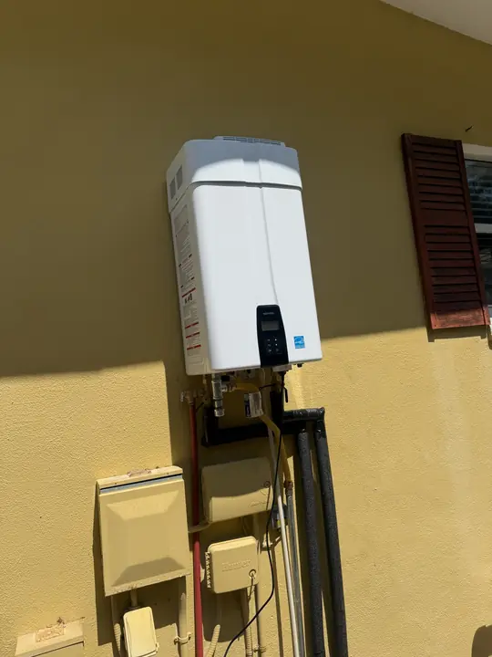 Outdoor tankless water heater mounted on a yellow stucco wall with insulated lines