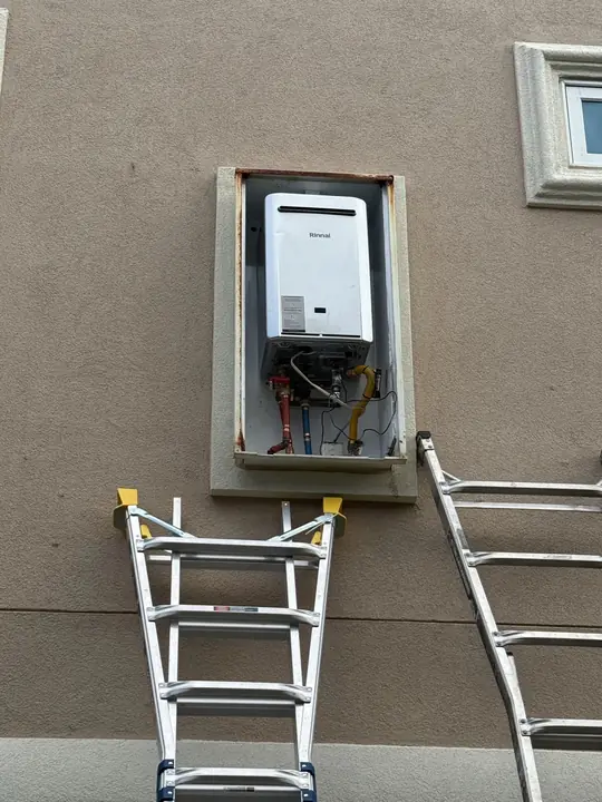 Tankless water heater inside a recessed wall box with gas and water connections visible