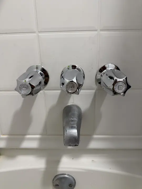 Three chrome tub and shower handles with tub spout on white tile