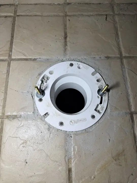 New white toilet flange with brass bolts set in a stone tile floor