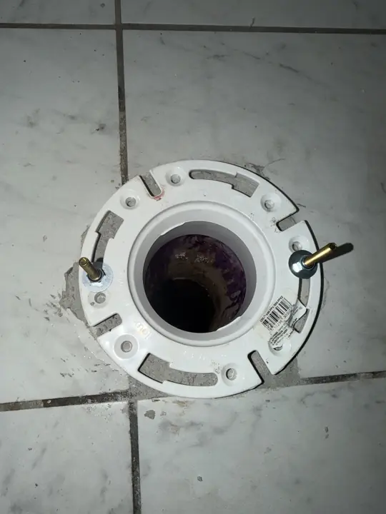 New white toilet flange with brass bolts set in a tile floor