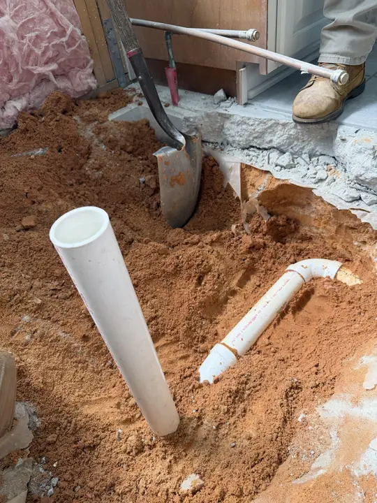 New PVC drain riser and fitting in a trench through a concrete floor