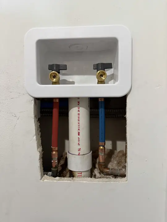 New recessed washing machine outlet box with two shutoff valves and red and blue supply lines in an open wall