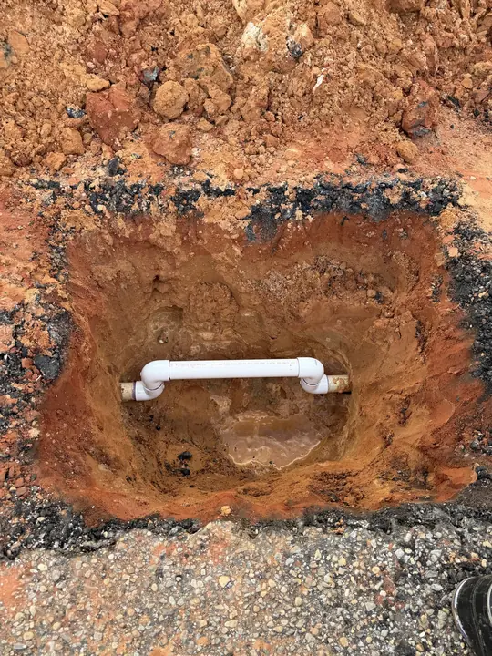 New white PVC water line section installed in a square excavation cut through pavement