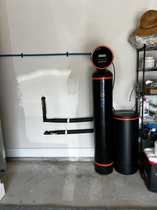 Water softener tank and brine tank installed against a garage wall with new piping