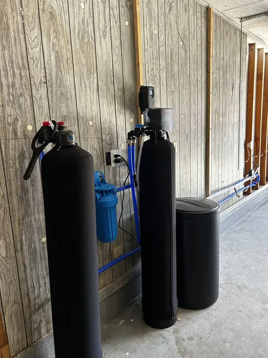 Side view of water treatment tanks, filter housing and brine tank with blue supply lines