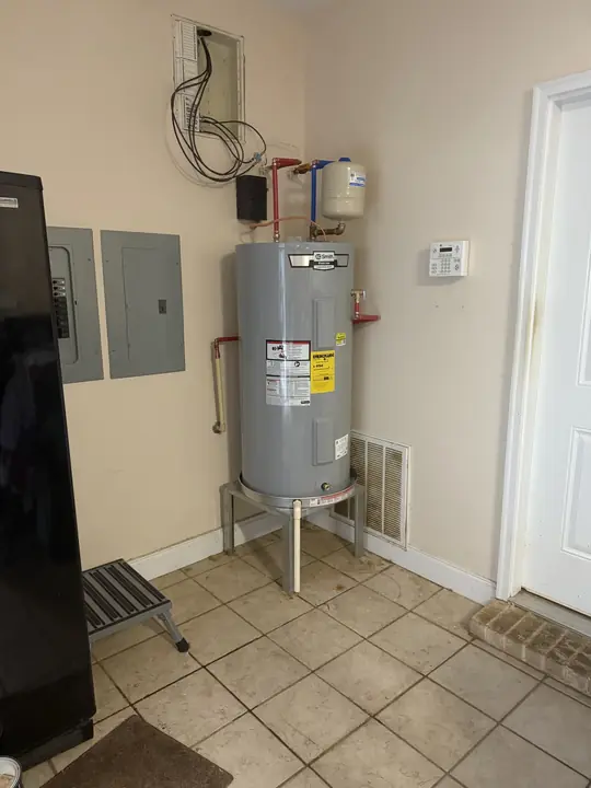 Electric water heater on a metal stand with a wall-mounted expansion tank in a garage