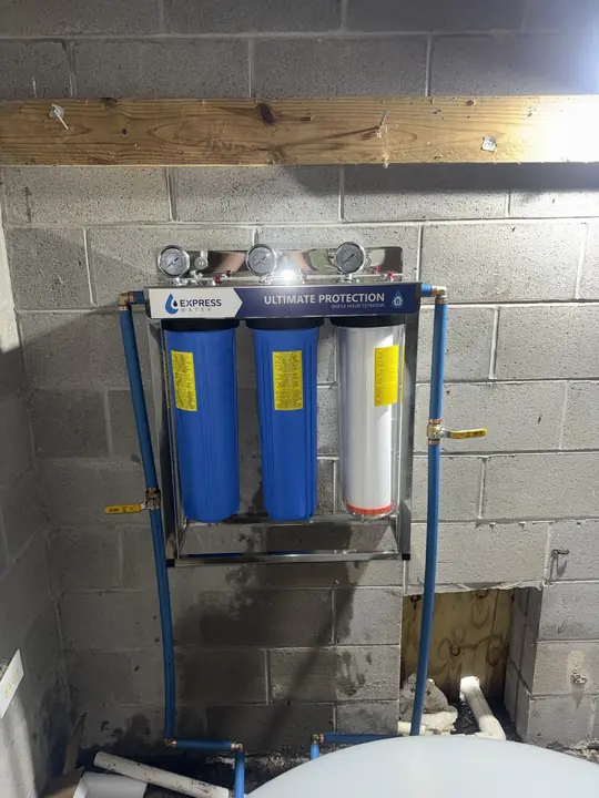 Three-stage whole-house water filtration system with pressure gauges mounted on a block wall