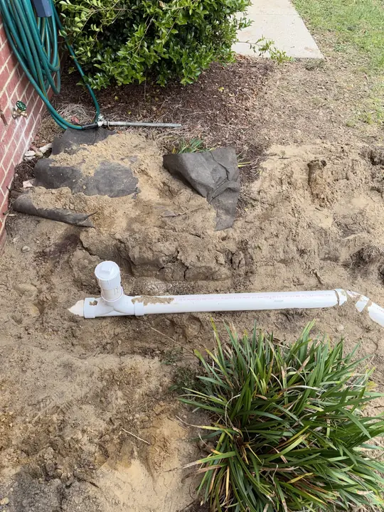 New white PVC sewer cleanout installed in an open trench beside a house